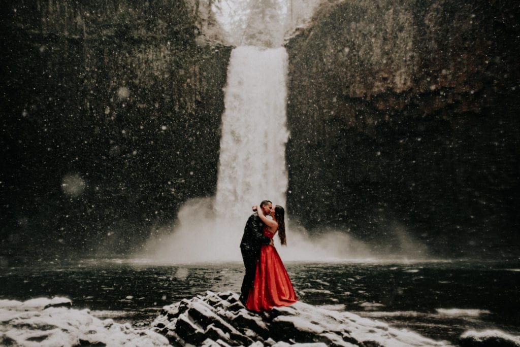 Melissa and Chase Pantoja kissing in front of a waterfall. Melissa is in a red gown and Chase is wearing a suit