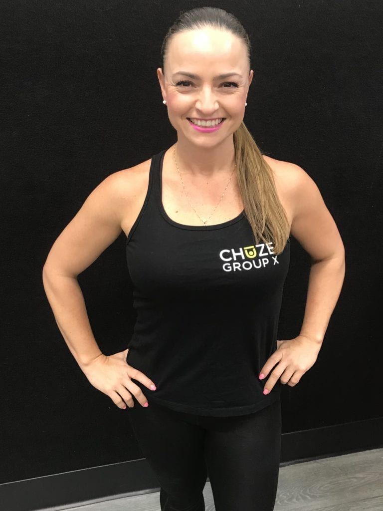 Instructor, Betty Layman, posing in front of a black wall wearing her Group X Chuze Fitness black shirt