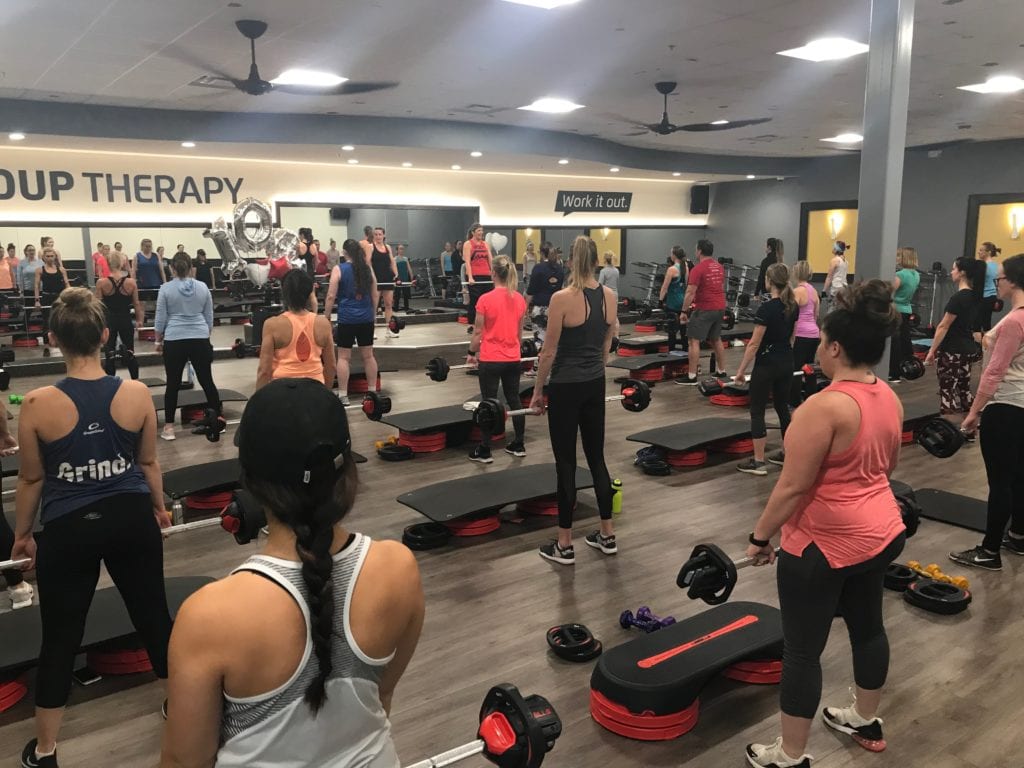 Instructor, Jamie Greaser, teaching a Les Mills on stage in front of a group exercise class at Chuze Fitness in Colorado.