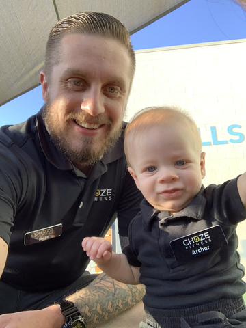 Nathan and, son, Archer Muzquiz outside at a Chuze Fitness location, both wearing their Chuze Fitness uniforms. 