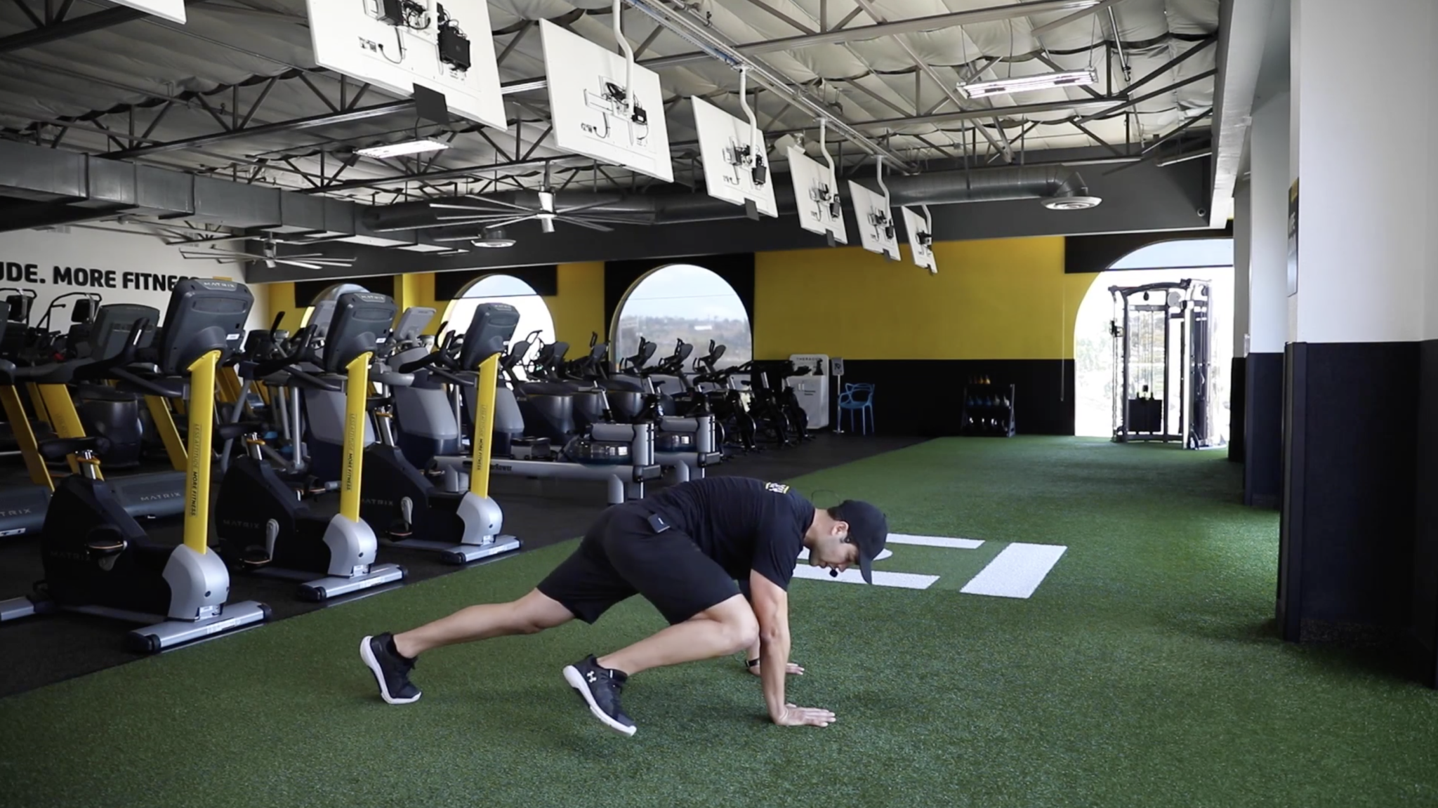 Coach Anthony, on iChuze Fitness, showing the Spiderman plank with one knee going toward the same side's elbow in a plank position