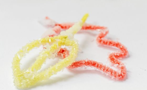 Image of one yellow and one orange pipe-cleaner covered in salt crystals 